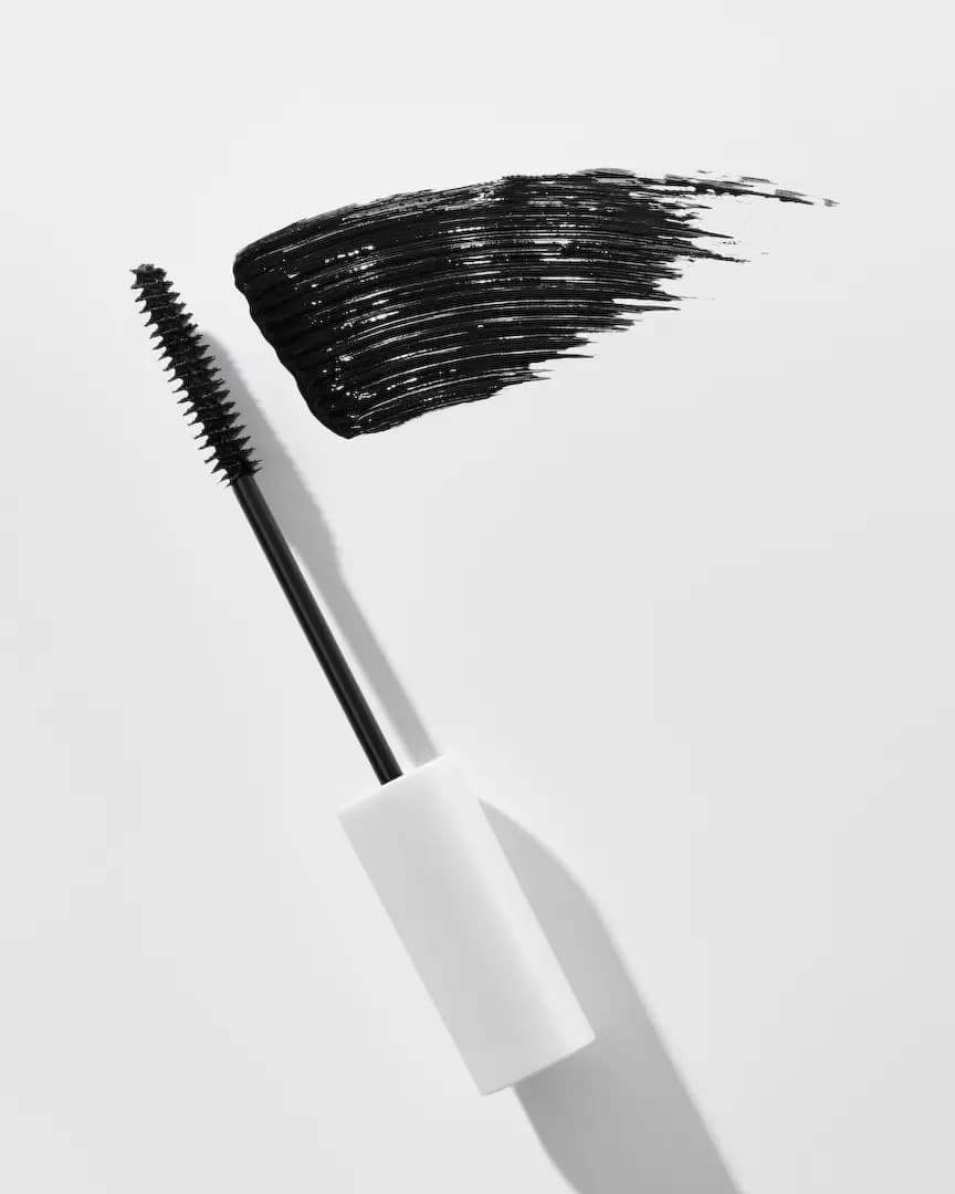 Spoolie wand on a white cap beside a shiny black mascara smear on a white surface