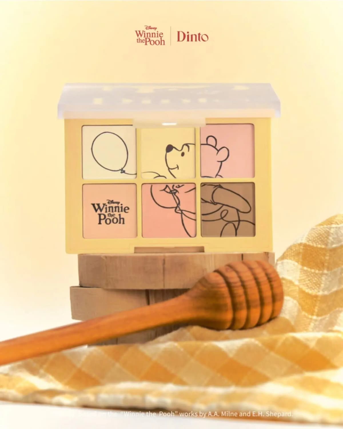 Dinto Blur-Finish Shadow 711 Winnie the Pooh eyeshadow palette in yellow case on wood slices beside a honey dipper