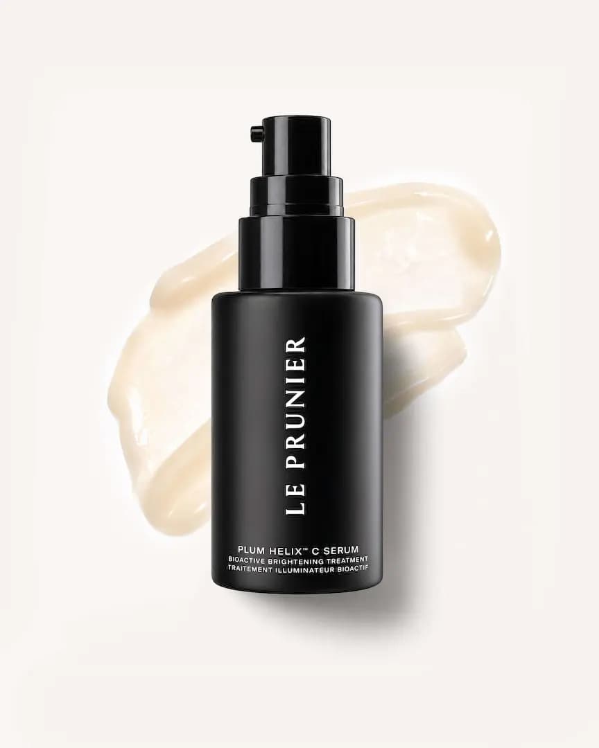 Black serum bottle laid over a broad, glossy swipe of ivory cream on an off-white background