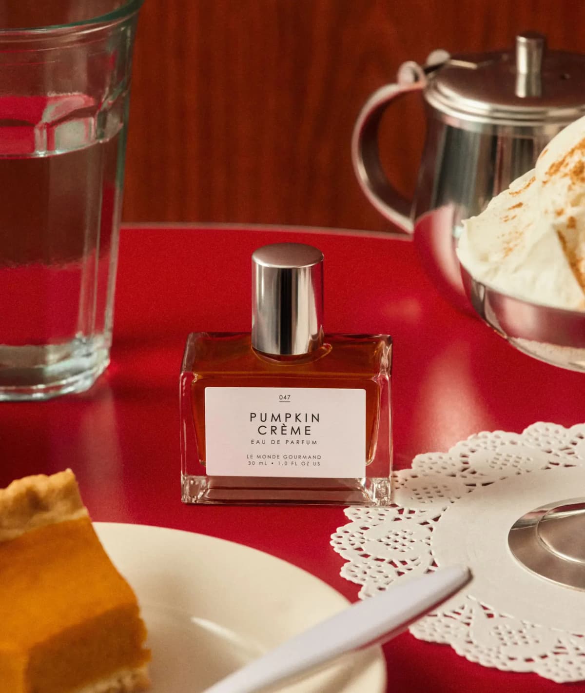 Pumpkin Crème bottle on a red diner table near pumpkin pie, a water glass and cinnamon-dusted whipped cream