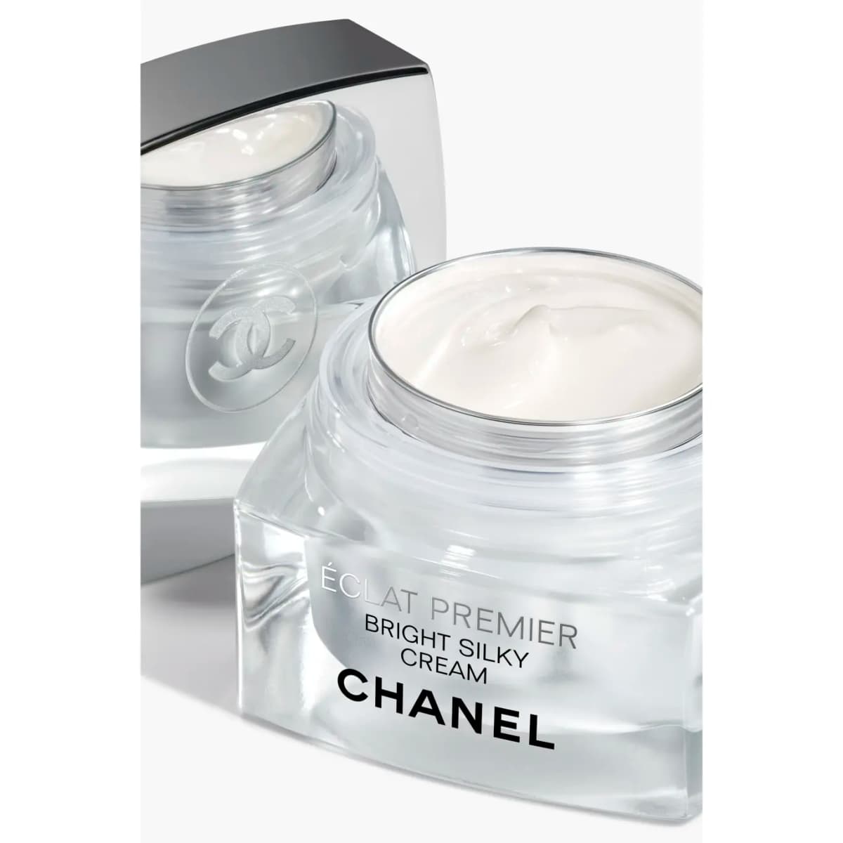 Close-up of an open Éclat Premier jar filled with white cream, beside a second jar showing an embossed CC logo