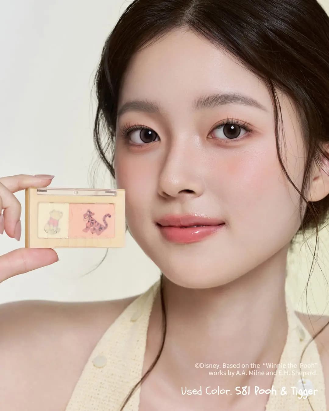 Model with rosy cheeks and peachy lids holds the S81 Pooh & Tigger dual blusher beside her face