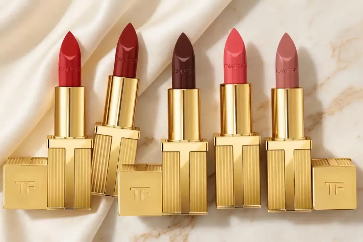 Five gold fluted Tom Ford lipsticks in red, brick, brown, coral and nude with TF caps on cream satin and marble