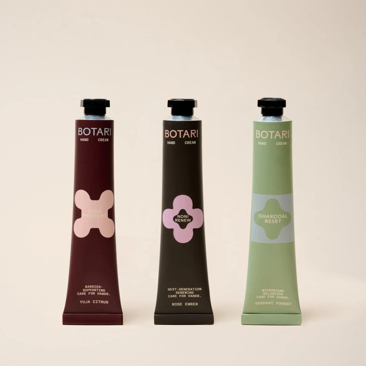 Three BOTARI mini tubes in burgundy Cica Protect, dark brown Noni Renew and sage green Charcoal Reset on a cream backdrop