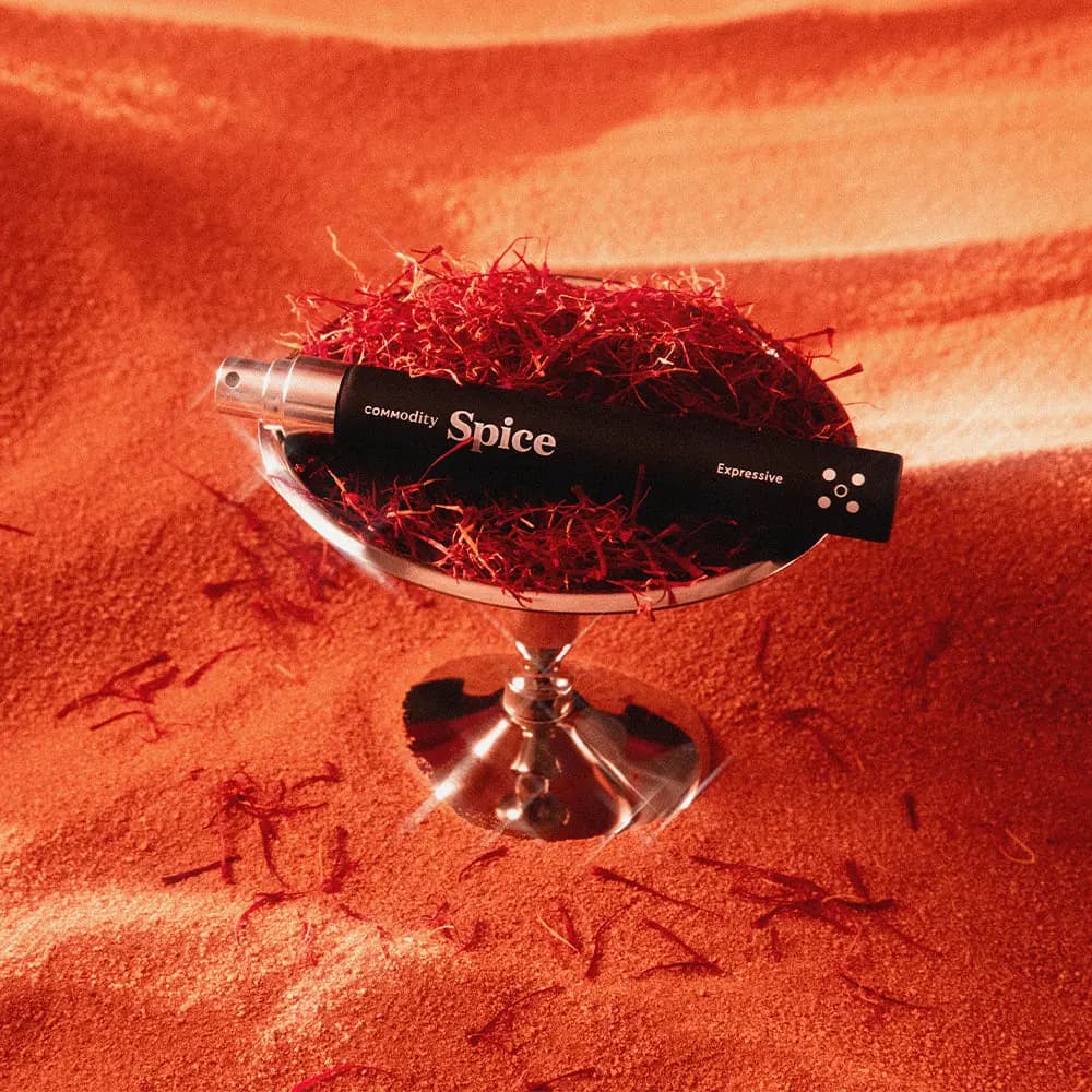 Black Commodity Spice Expressive travel spray resting on saffron threads in a silver pedestal dish on orange sand