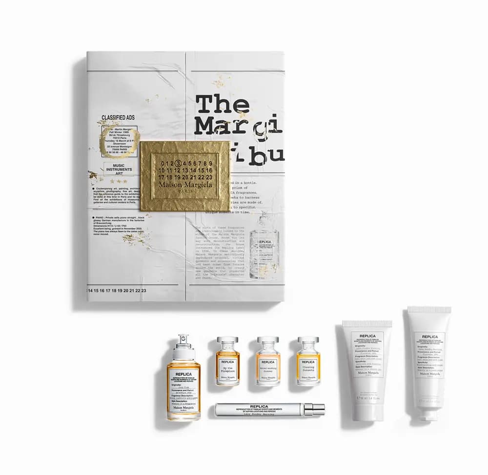 Newspaper-print calendar box with gold Margiela label above a flat lay of perfume bottles, travel spray and two white tubes