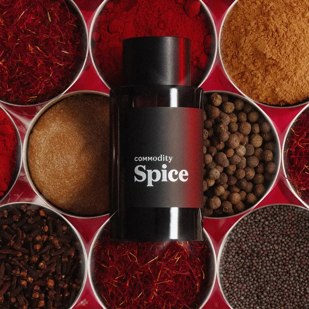 Black Commodity Spice bottle lying on bowls of saffron, red chilli powder, cinnamon, allspice, cloves and mustard seeds