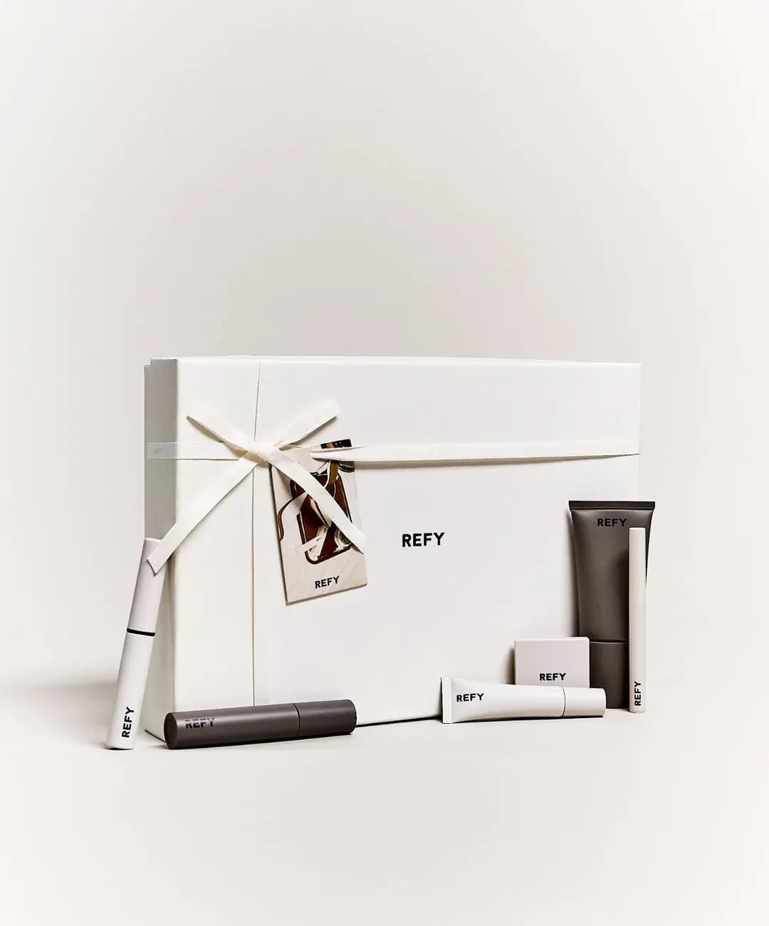 Ribbon-tied cream REFY gift box standing upright with the makeup products leaning against its front