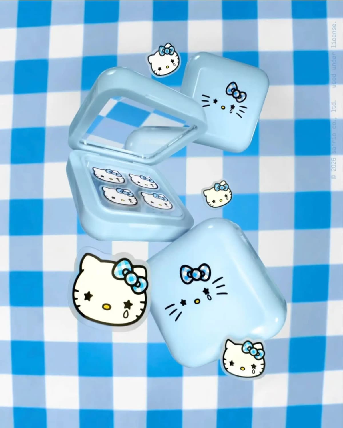 Light blue compacts, one open with gingham-bow Hello Kitty patches, over a blue gingham background