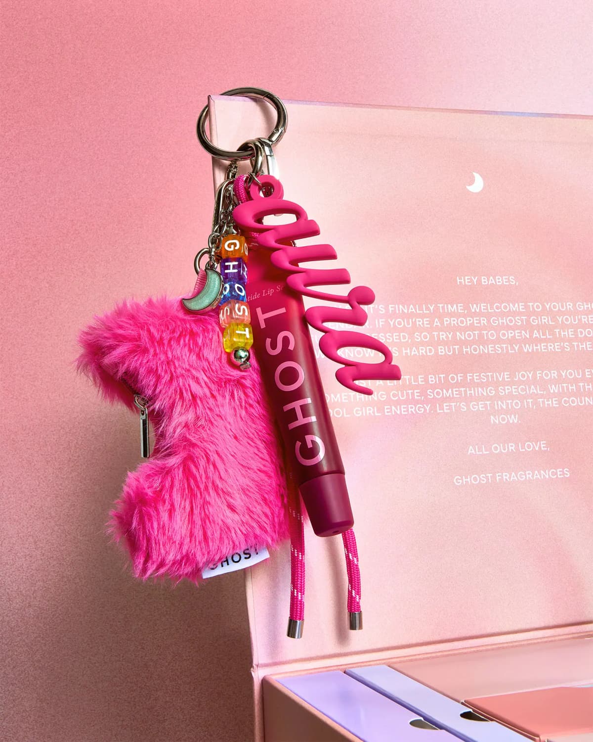 Hot pink fluffy keyring with GHOST letter beads, aura charm and Ghost lip serum hanging from the calendar lid