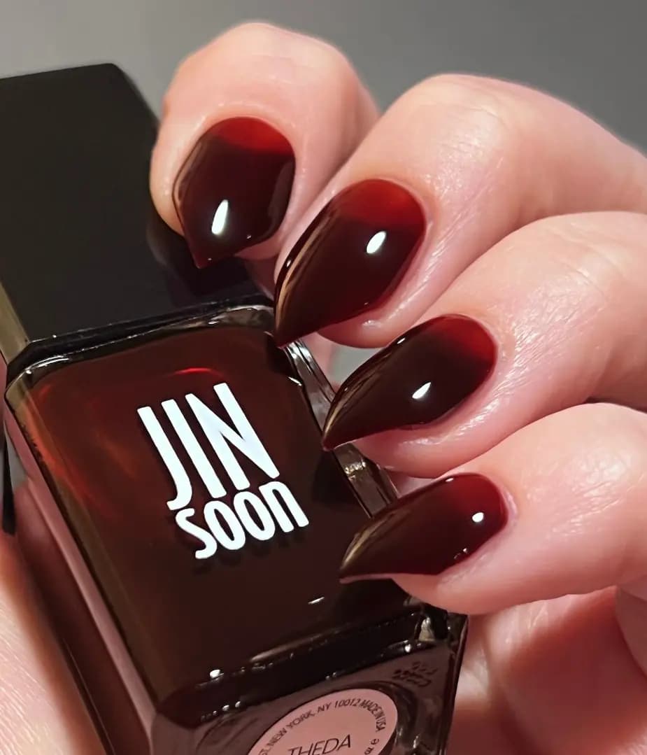 Hand with glossy translucent blackened red nails holding a JINsoon bottle labelled Theda