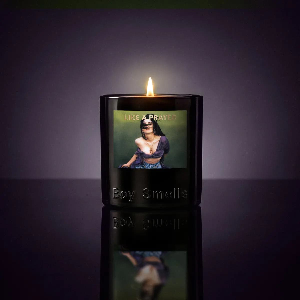 Lit Like a Prayer candle on a reflective surface against a dim violet background