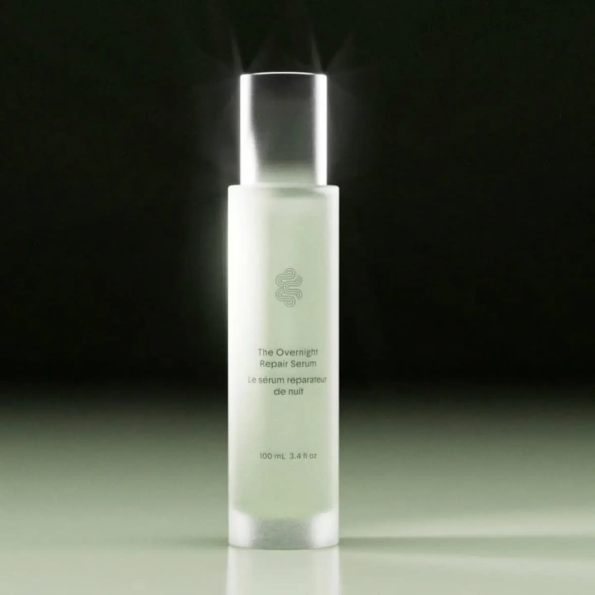 Frosted pale green Crown Affair The Overnight Repair Serum bottle, 100 mL, with silver cap glowing against black