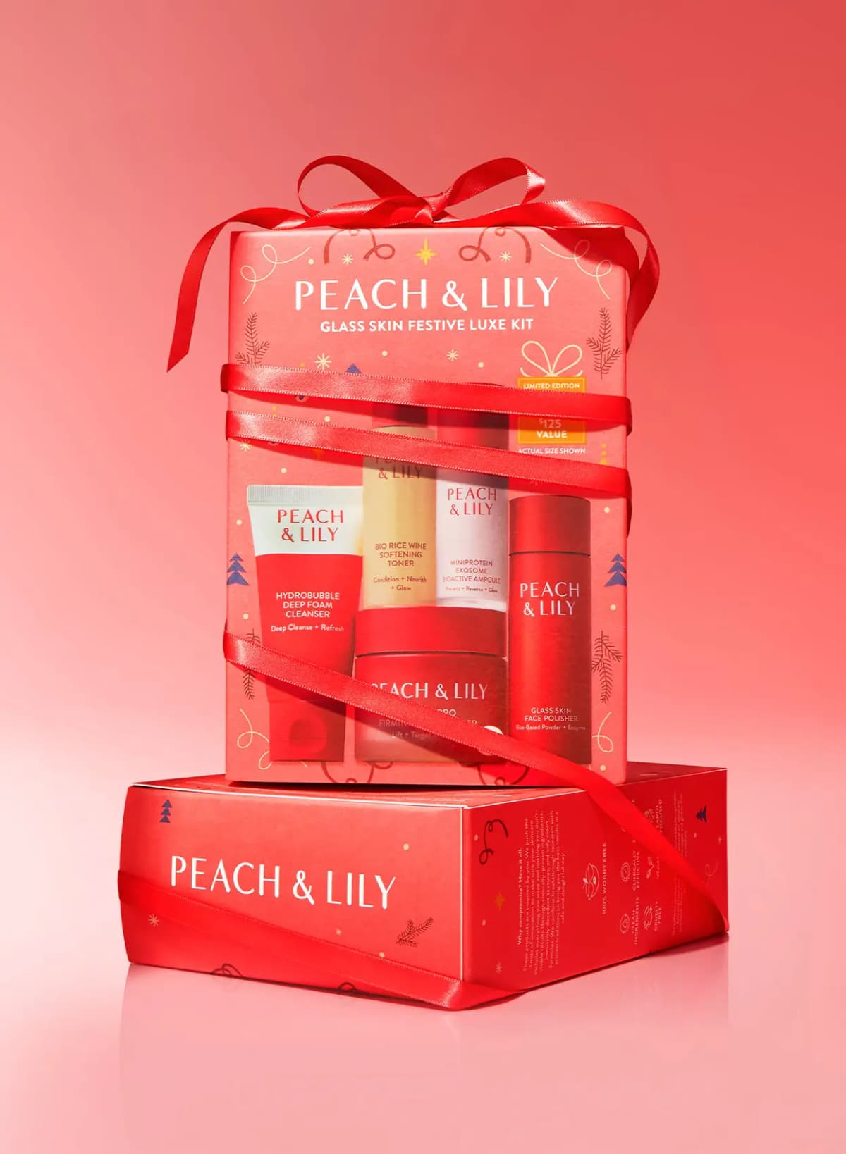 Glass Skin Festive Luxe Kit box tied with red satin ribbon, resting on a red Peach & Lily box against a red gradient