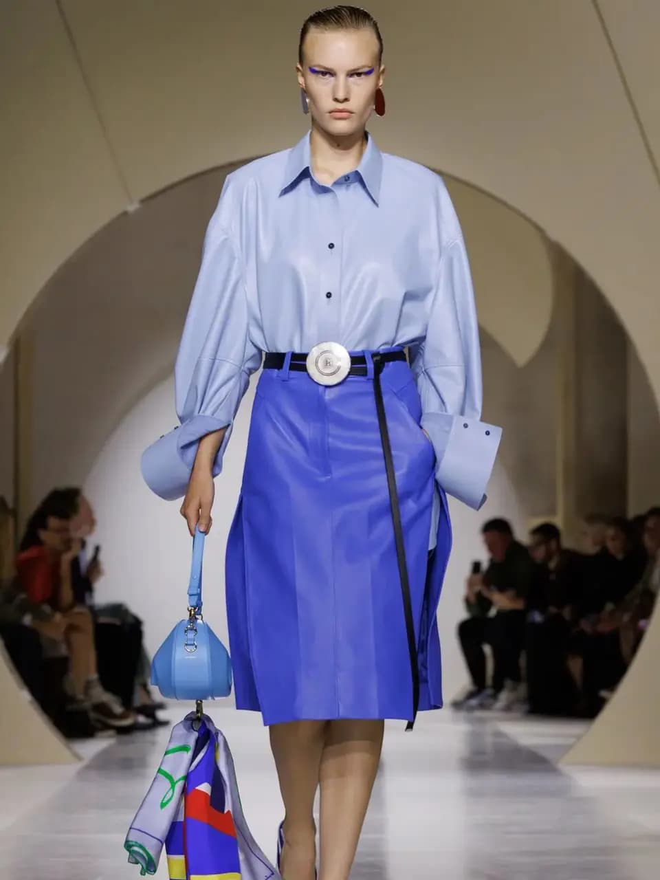 Runway model in a pale blue leather shirt and cobalt skirt with a silver compact buckle on a black belt