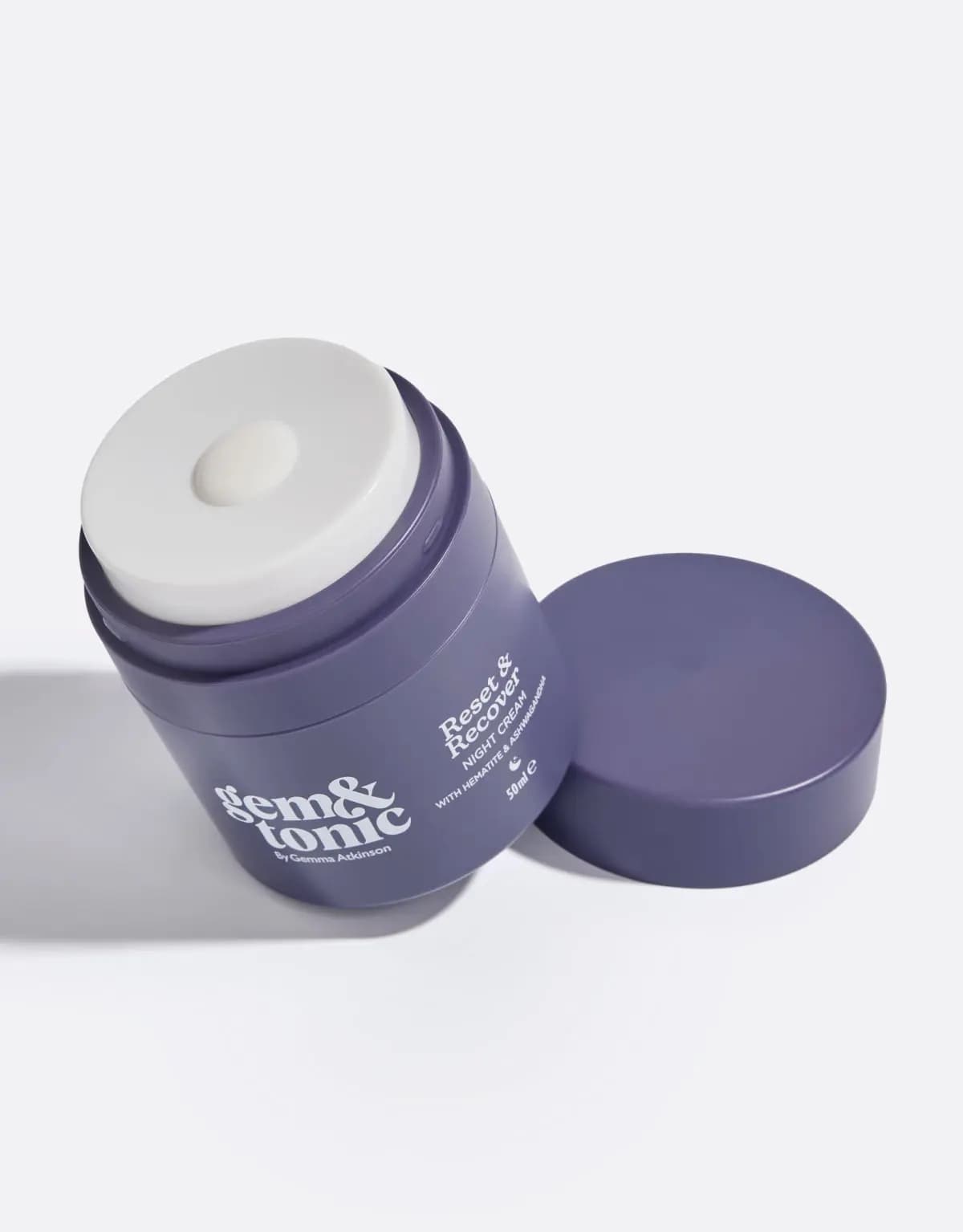 Open purple Gem & Tonic jar showing a white pump top with a dot of cream, its lid lying beside it on white