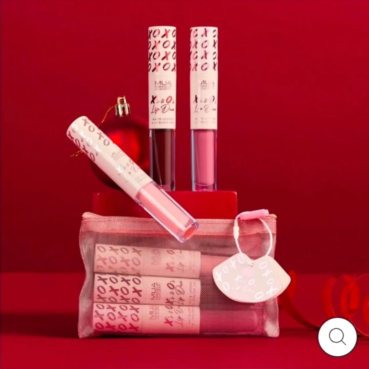 Three MUA X's & O's Lip Duos in brown, berry and nude pink above a pink mesh pouch on a red backdrop.