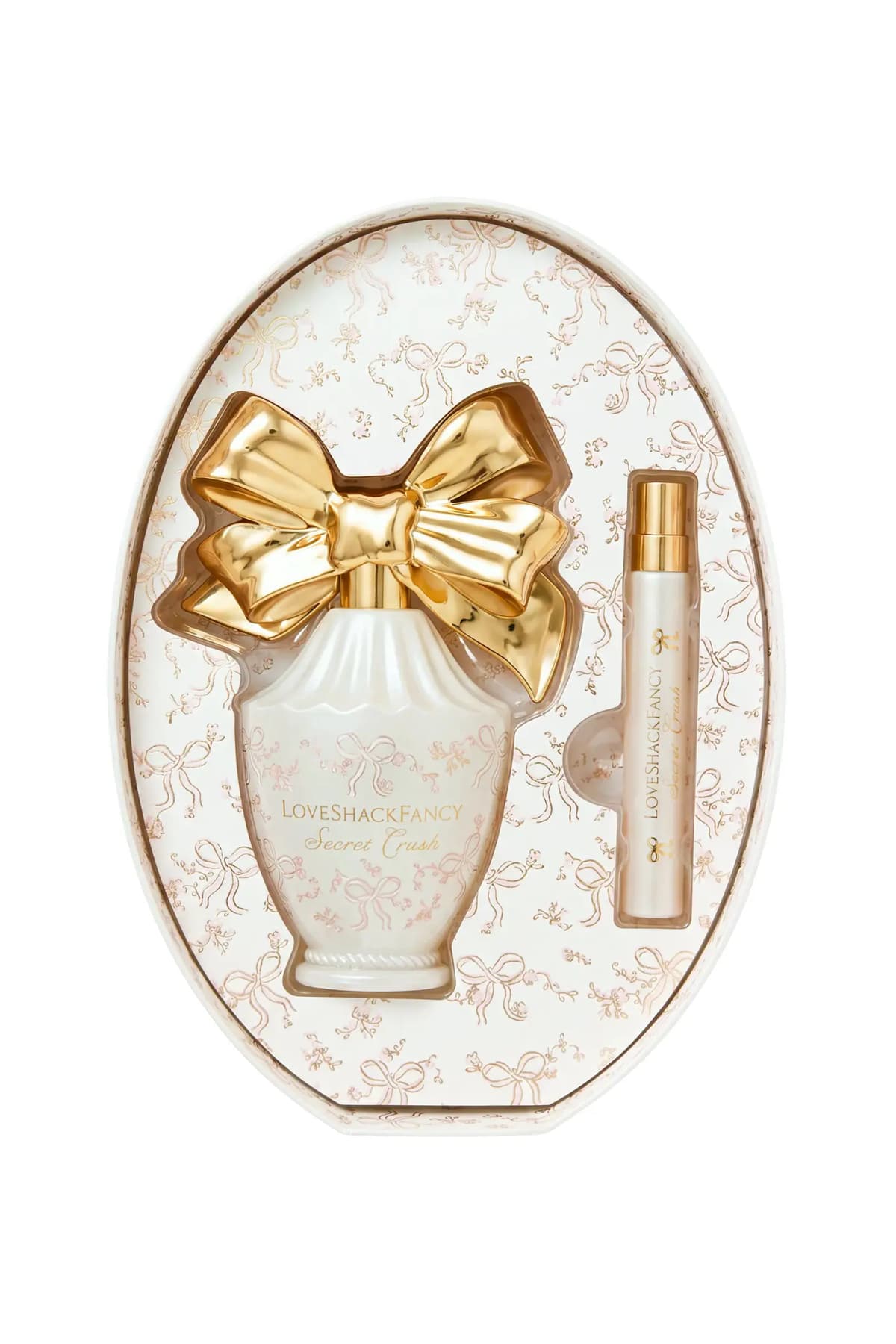 Open oval keepsake box holding the Secret Crush bottle with gold bow cap and slim travel spray in a pink-and-gold bow print