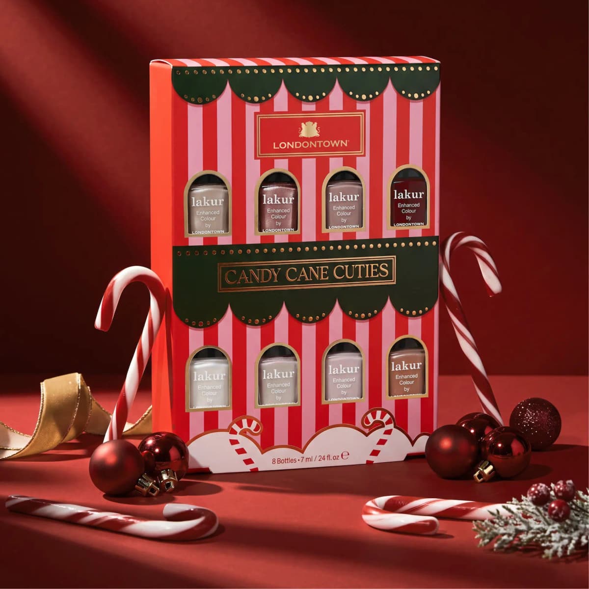 Candy Cane Cuties box standing among candy canes, red baubles, gold ribbon and frosted berries on red