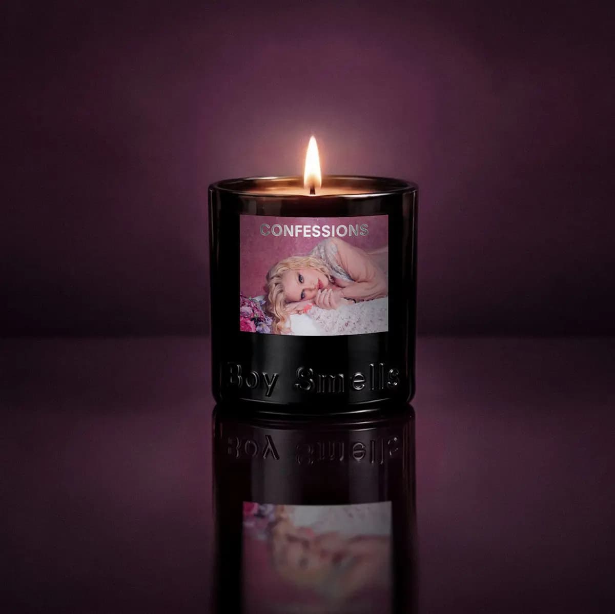 Lit Confessions candle glowing against a deep plum background with its label reflected below