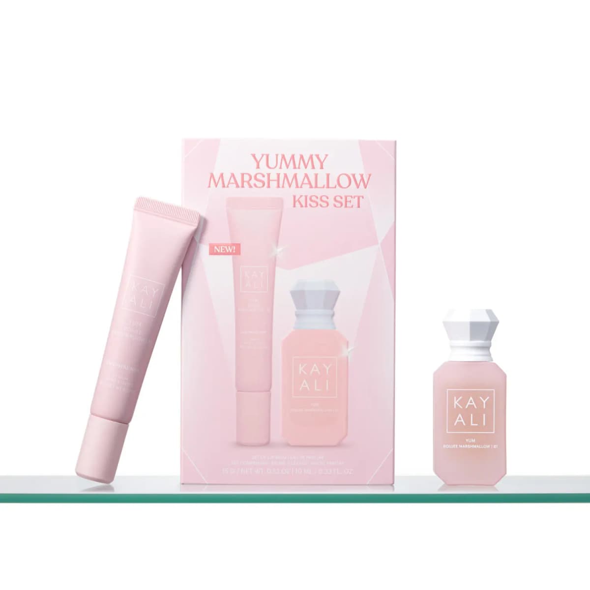 Pink lip balm tube leaning on the Marshmallow Kiss Set box with the white-capped perfume bottle on a glass shelf