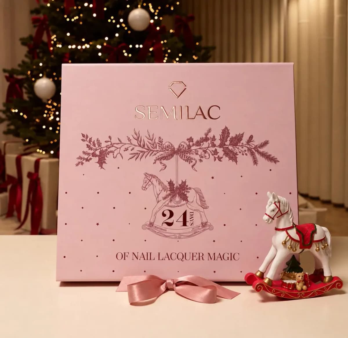 Semilac 24 Days of Nail Lacquer Magic Advent Calendar in a pink box with a rocking horse print, beside a Christmas tree