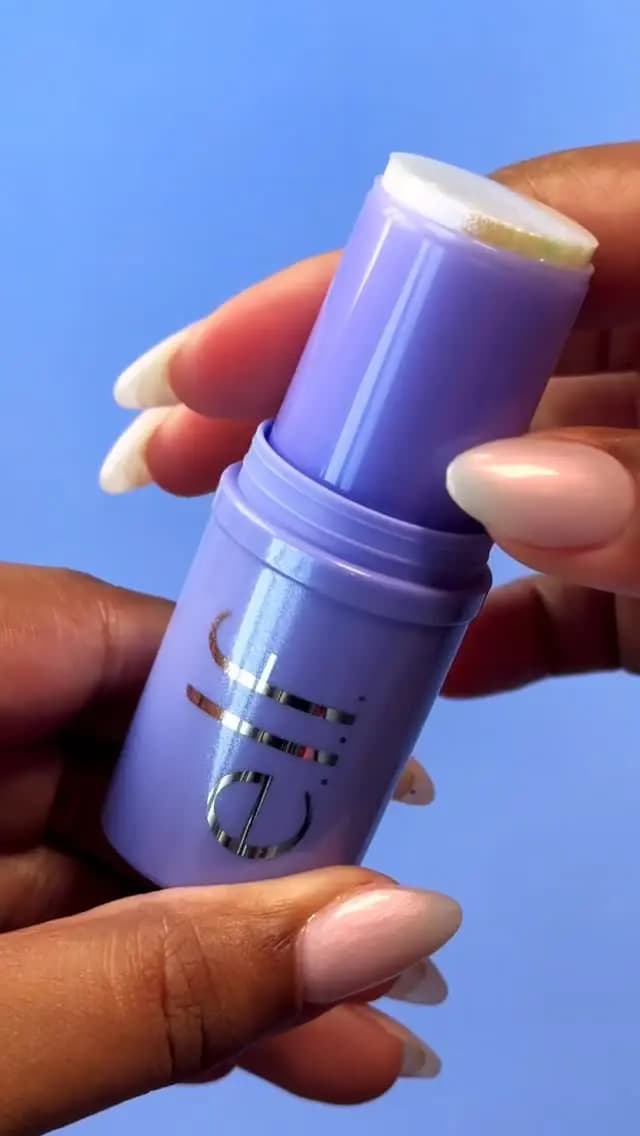 Hands with long nails hold an open lilac twist-up hair stick against a bright blue background.