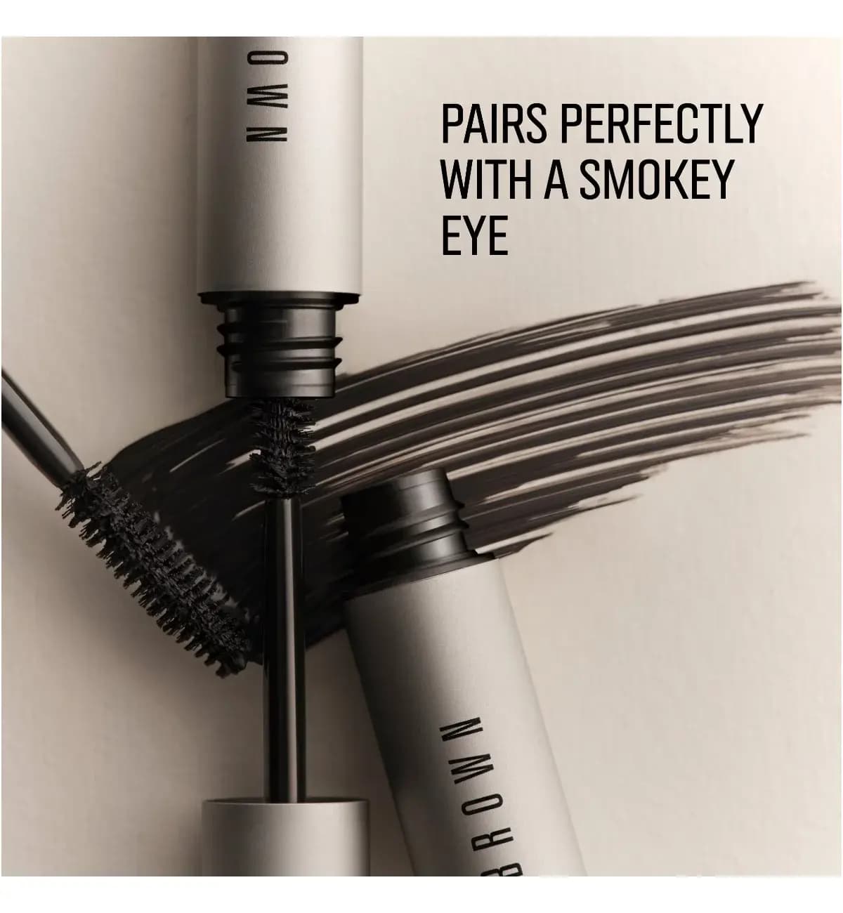 Two silver mascara tubes with black bristle wands over a dark mascara swatch, text: pairs perfectly with a smokey eye