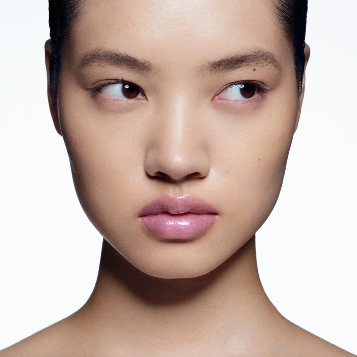 Model glancing sideways with a bare-skin look and glossy, sheer lilac-pink lips