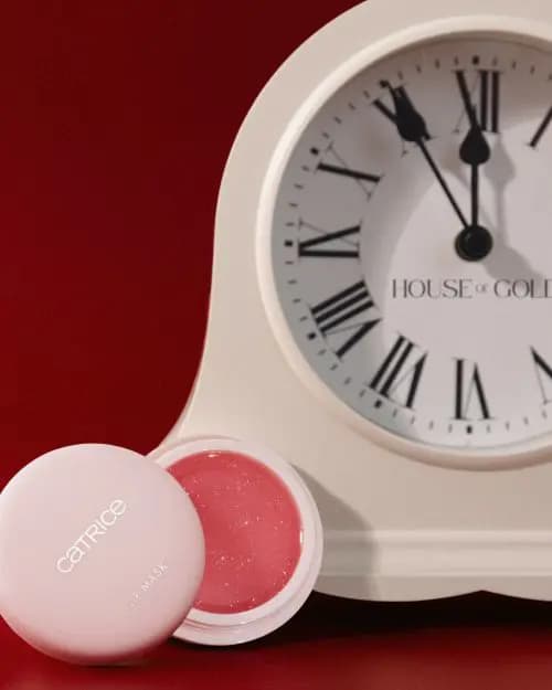 Open pink Catrice Lip Mask with shimmery rosy balm in front of a cream House of Gold mantel clock near midnight