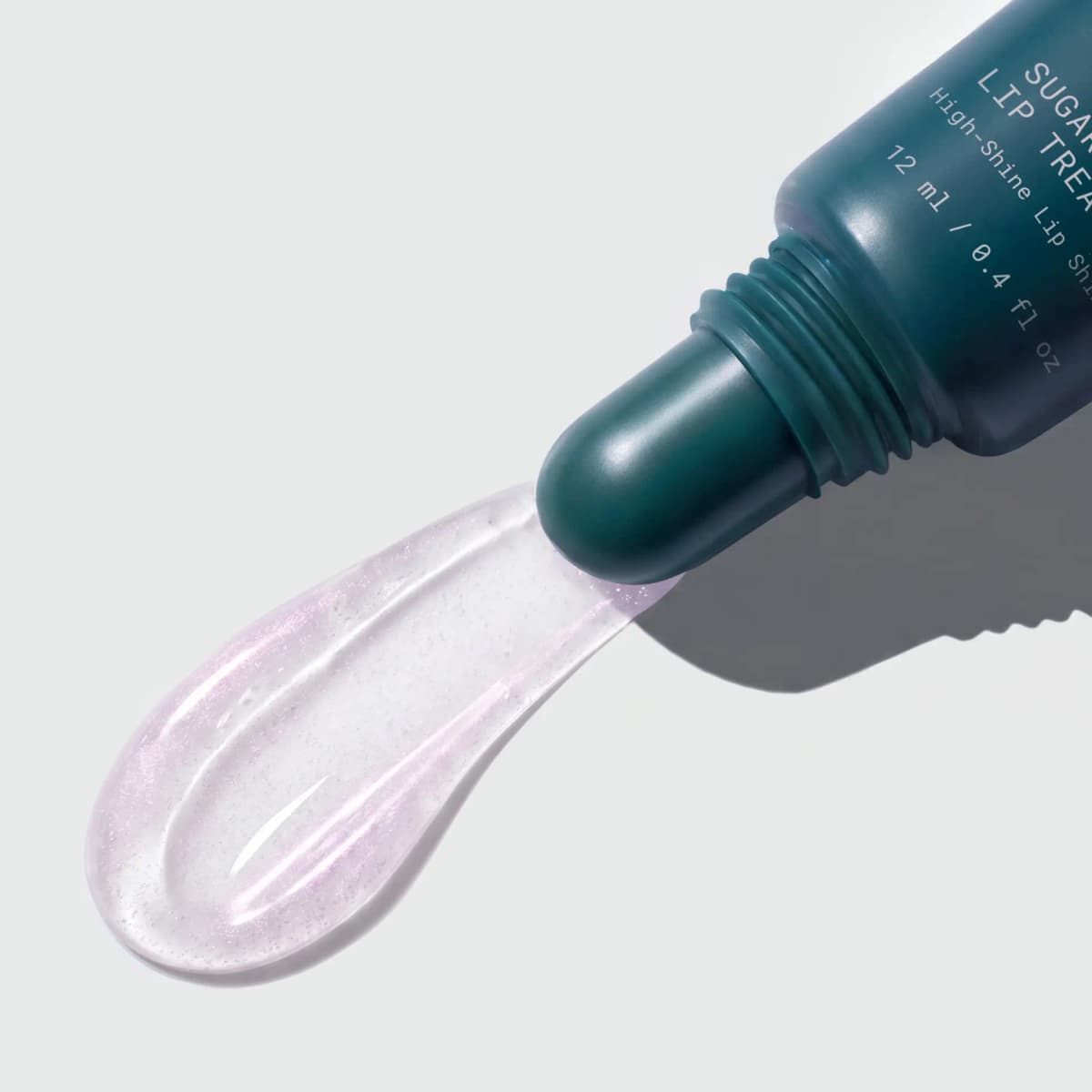 Sheer swatch of lilac-shimmer lip gloss squeezed from the teal tube's rounded tip