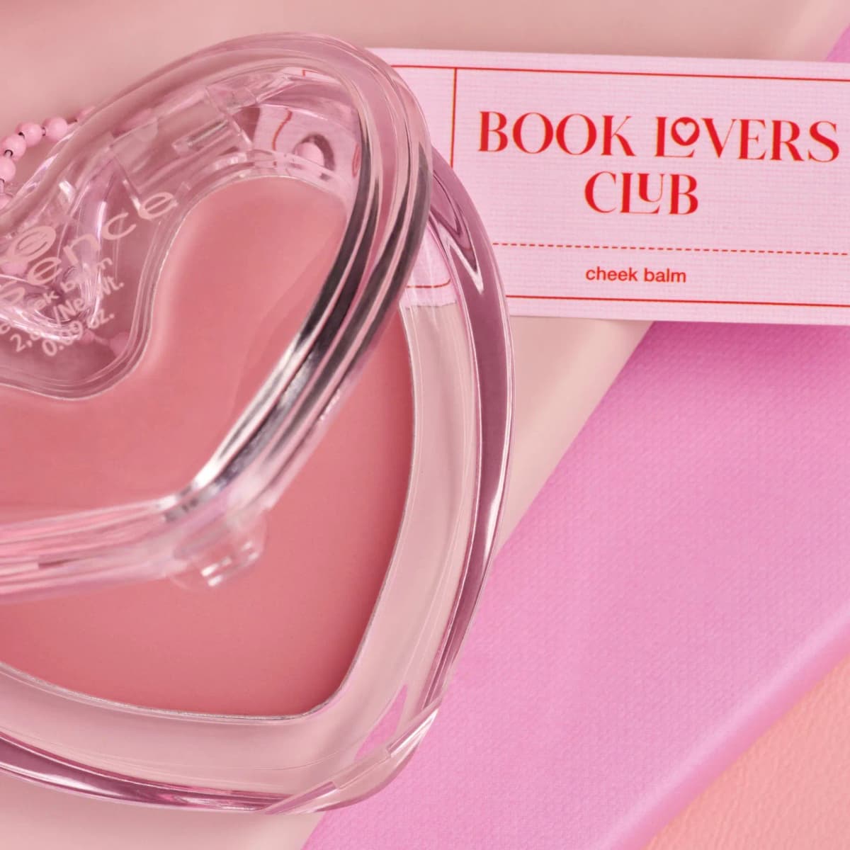 Close-up of mauve cheek balm under a clear heart lid next to a Book Lovers Club cheek balm tag