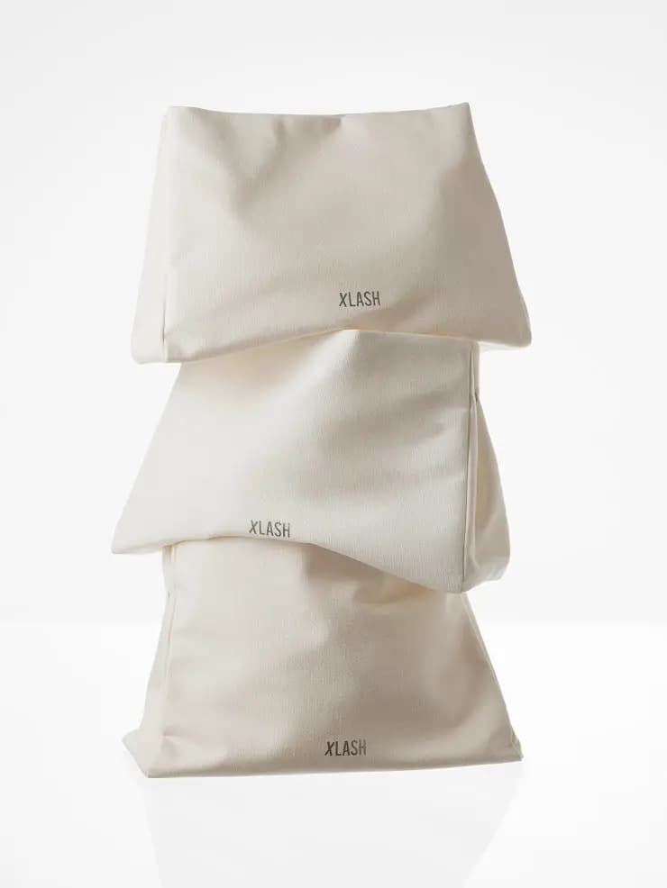 Three cream Xlash cotton pouches stacked on top of one another against a white background