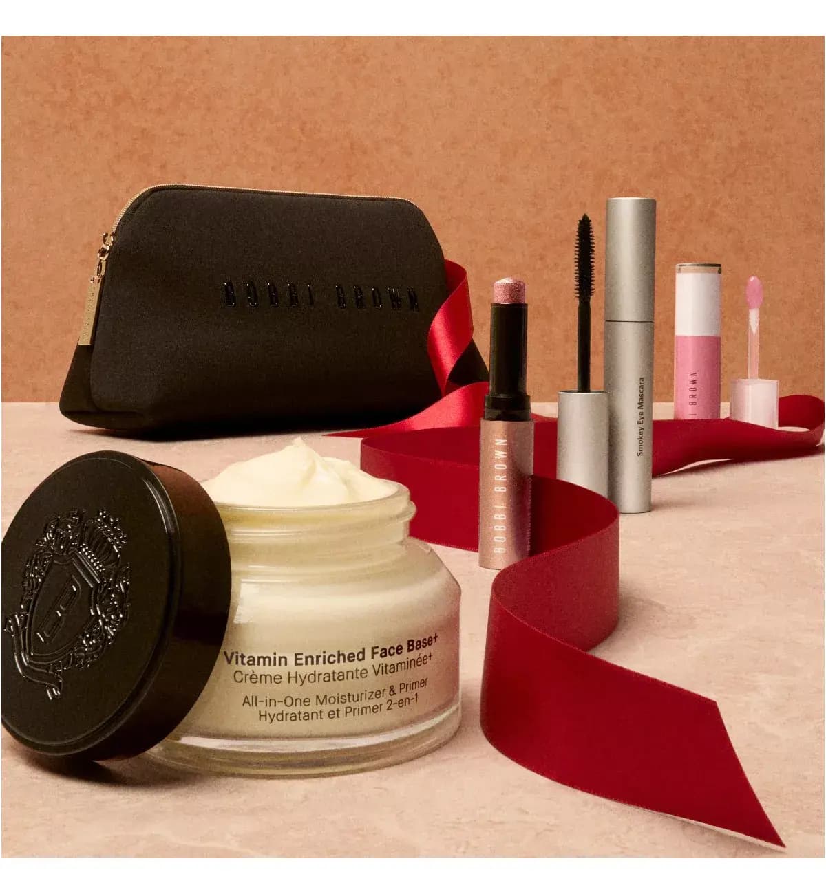 Black Bobbi Brown bag with open Vitamin Enriched Face Base+ jar, pink shimmer stick, Smokey Eye Mascara, gloss and red ribbon