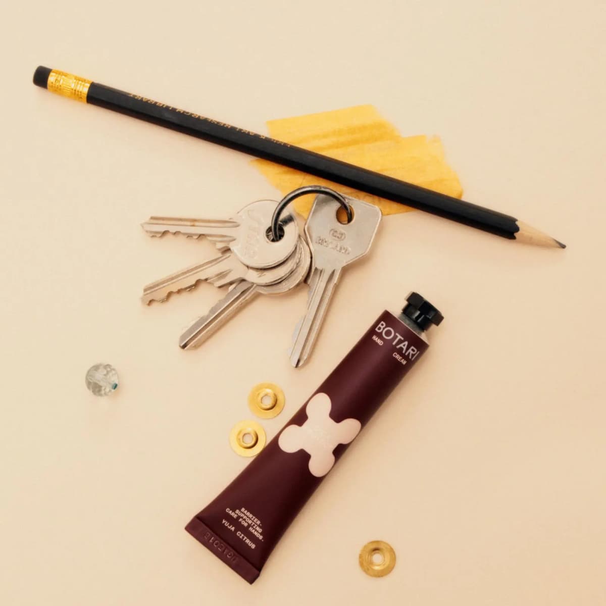 Burgundy BOTARI Cica Protect Yuja Citrus mini tube lying beside a set of keys, a black pencil and brass washers