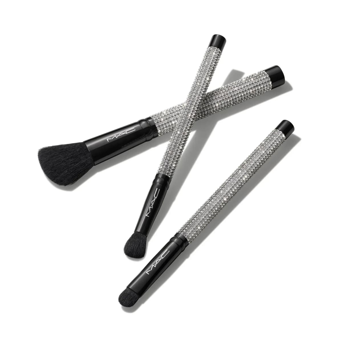 Three M·A·C makeup brushes with black ferrules and rhinestone-encrusted silver handles: angled face and two eye brushes.