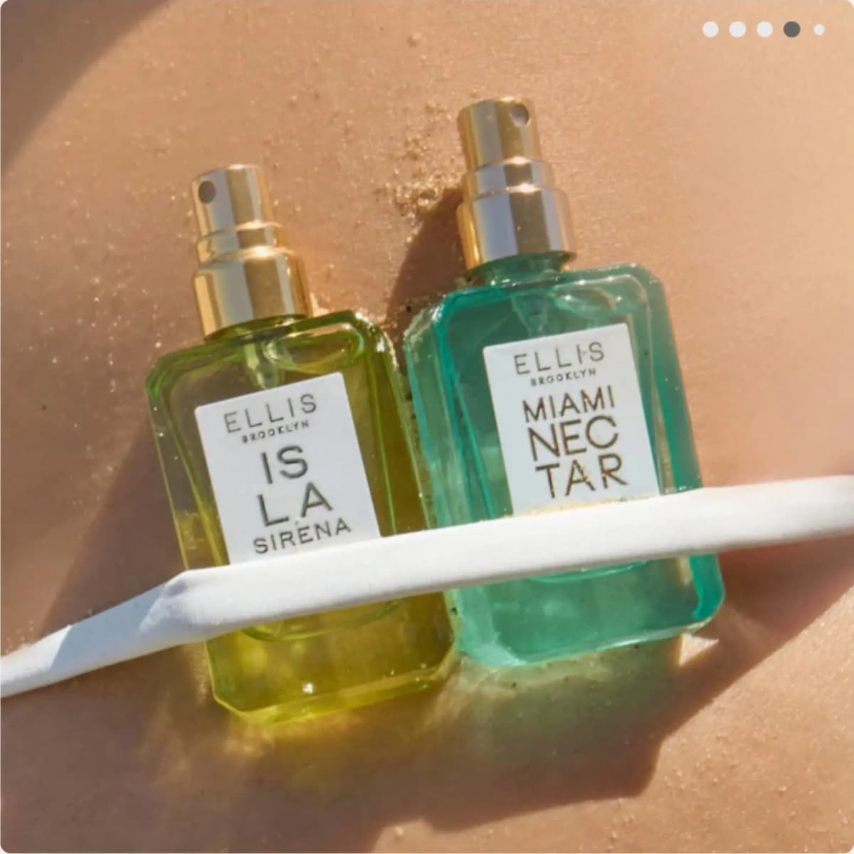 Uncapped lime and aqua mini bottles with gold sprayers tucked under a white bikini strap on sandy, sunlit skin