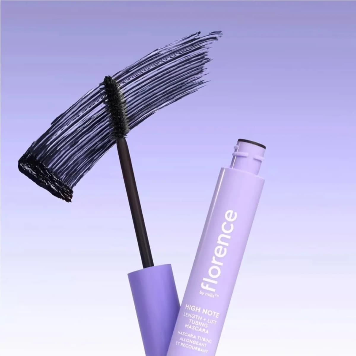 Open lilac mascara tube and wand in front of a dark black swatch on a lavender gradient