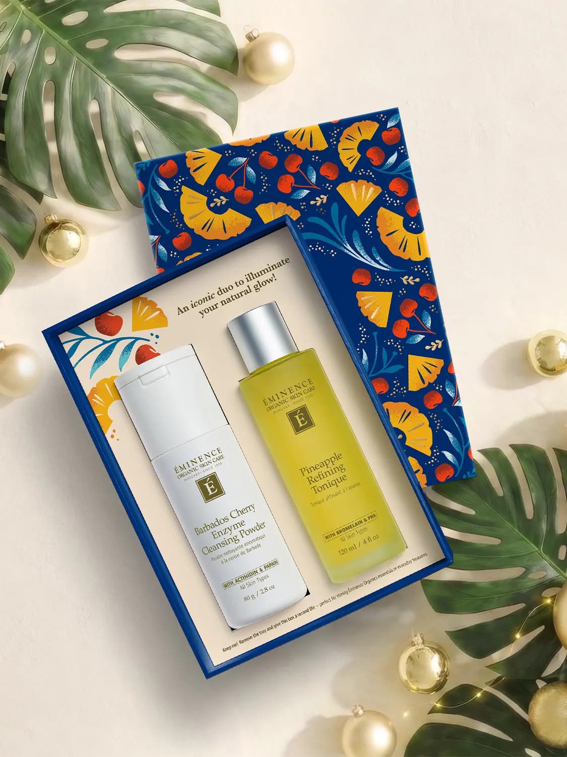 Open box with white Barbados Cherry Enzyme Cleansing Powder and yellow Pineapple Refining Tonique beside gold baubles