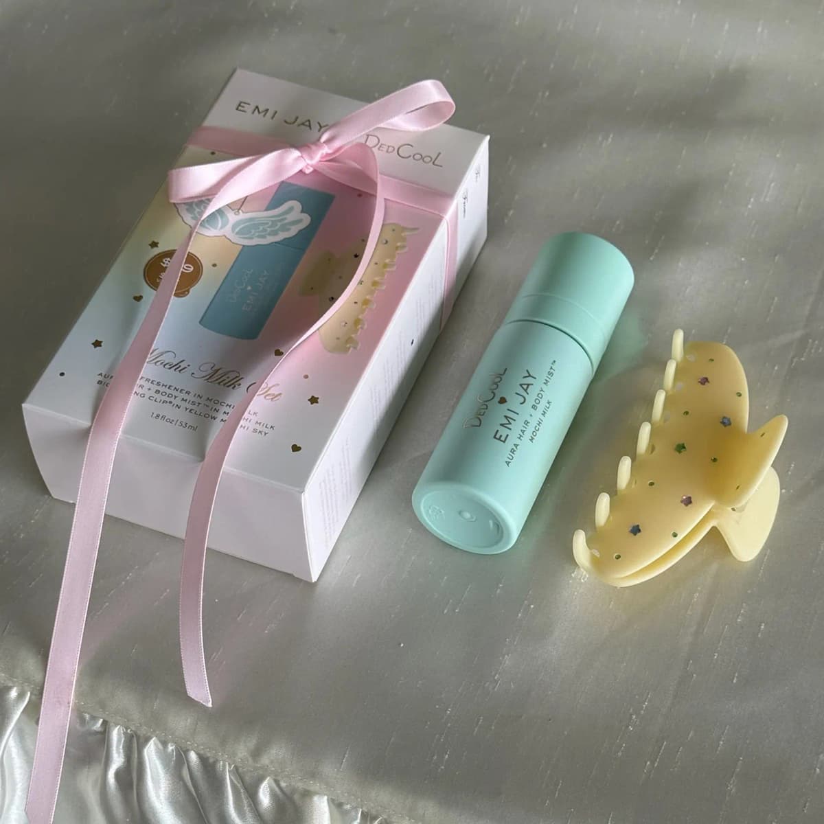 Gift box tied with a pink satin ribbon next to the mint mist bottle and pale yellow claw clip on ivory silk
