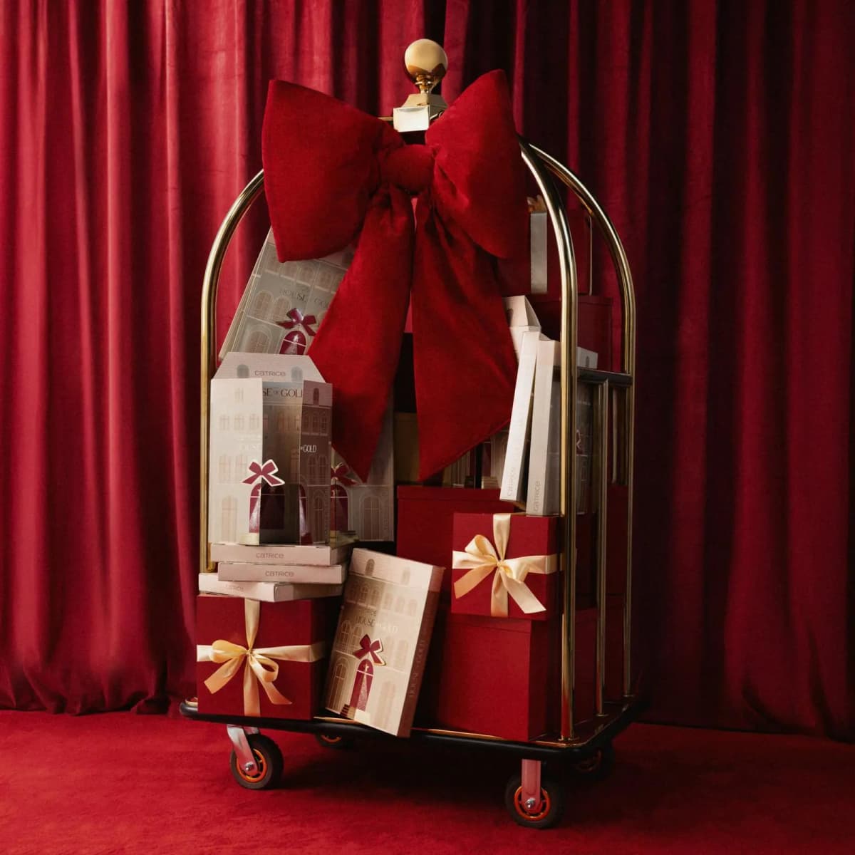 Gold luggage trolley with a huge red velvet bow, stacked with House of Gold calendars and red gift boxes