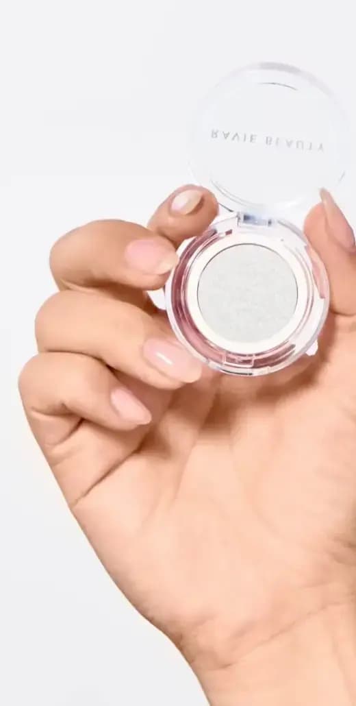 Hand holding an open Ravie Beauty compact of pale pearly white shimmer eye topper