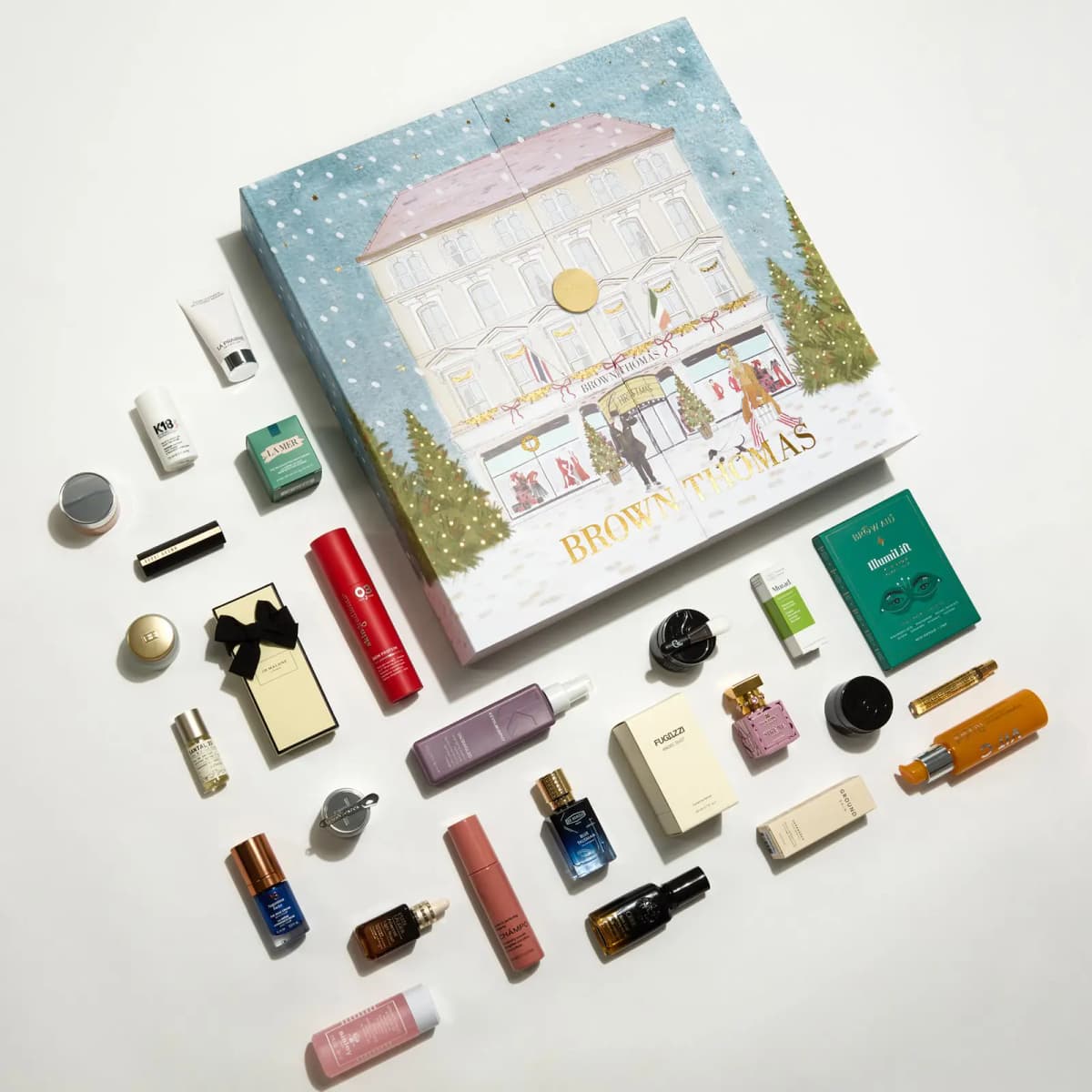 Flat lay of the closed illustrated calendar box surrounded by assorted beauty products including K18 and La Mer