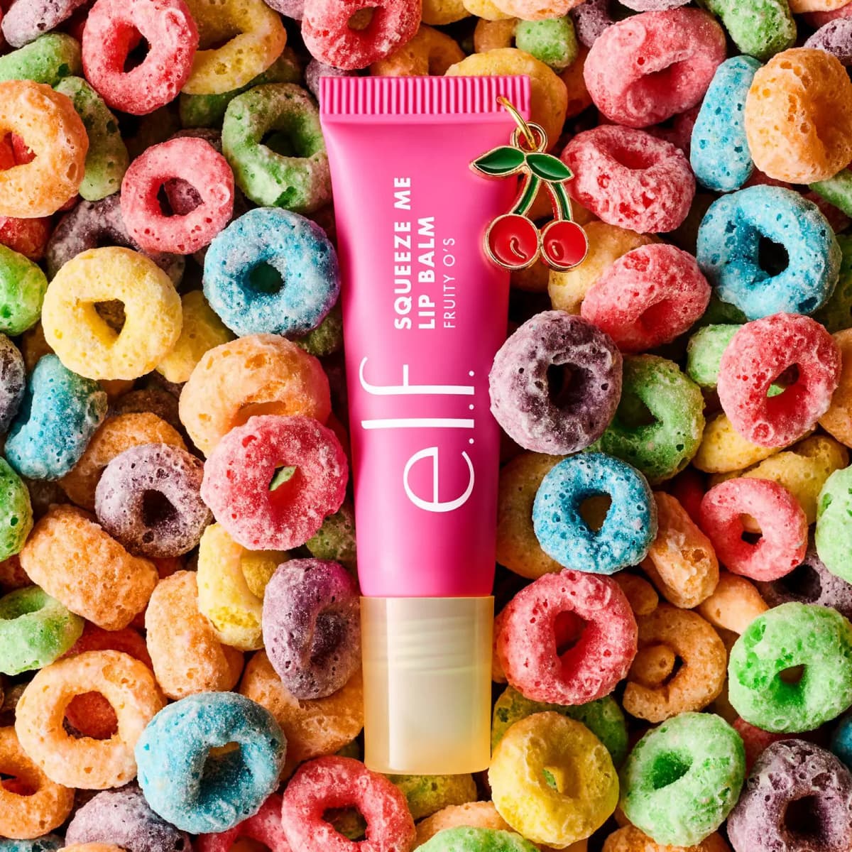 Pink Fruity O's lip balm with cherry charm lying on a pile of colourful fruity ring cereal
