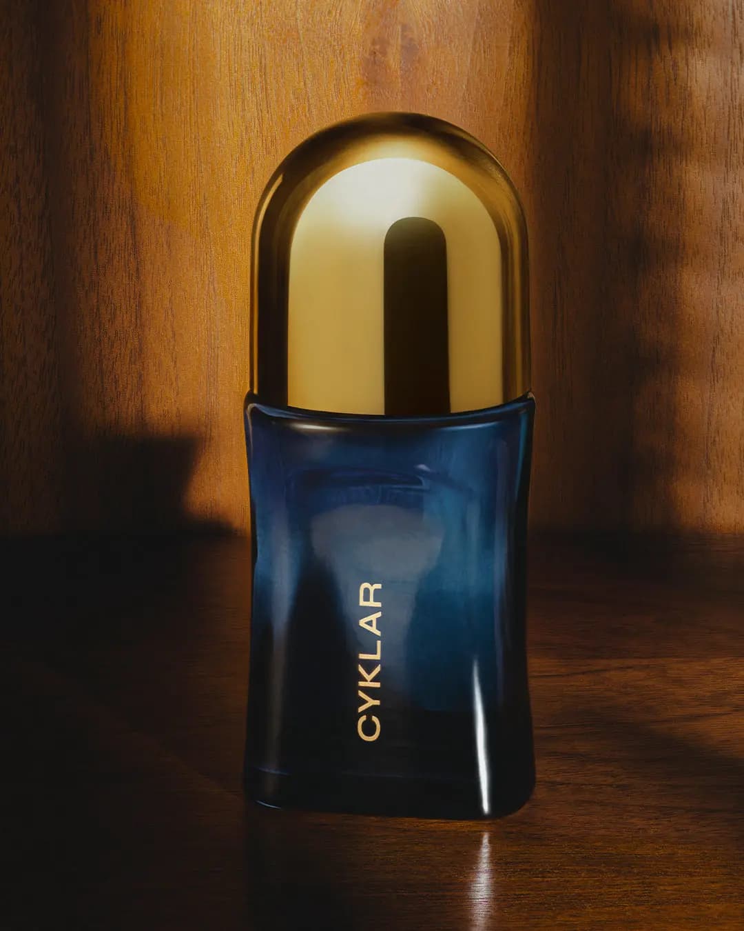 Deodorant with gleaming gold cap on a wooden surface, warm sunlight and leafy shadows behind
