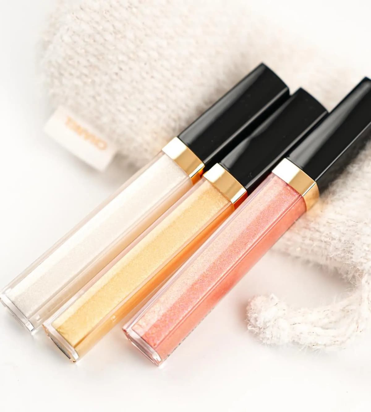 Chanel Holiday 2026 white-silver, golden and peach-pink lip glosses on a tweed pouch