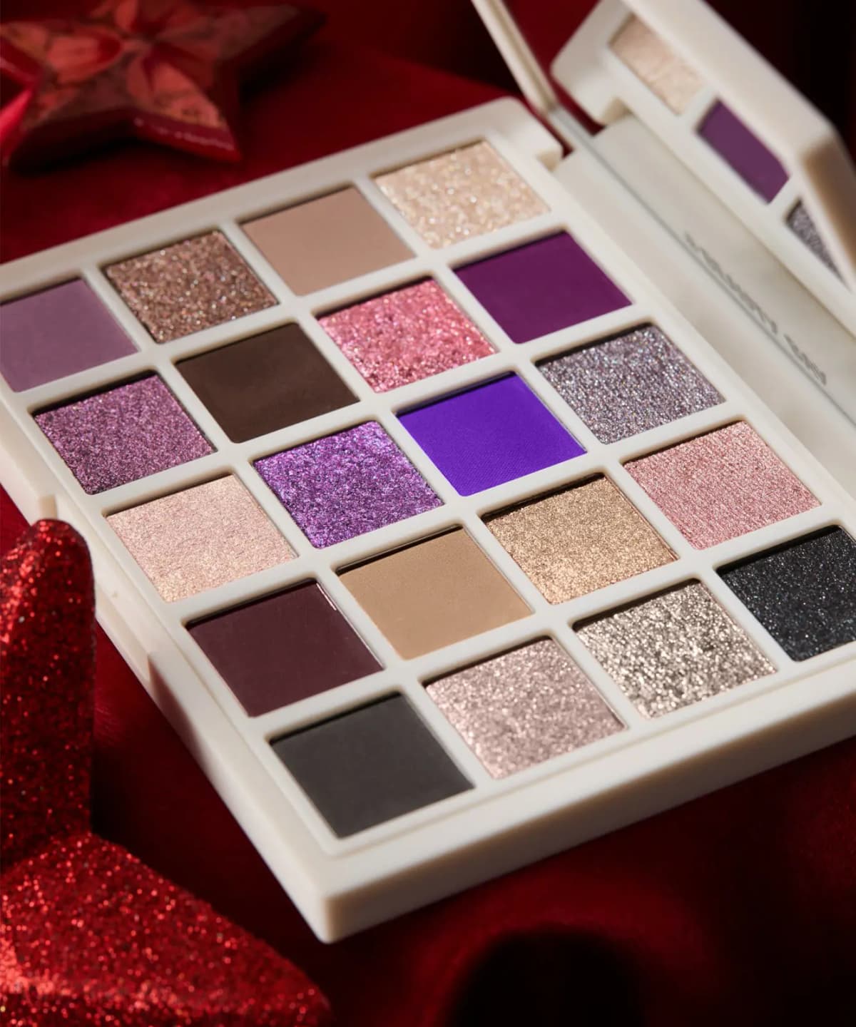 Close-up of palette pans showing glittery pinks and purples, a bright violet matte, mauves, browns and sparkly silver