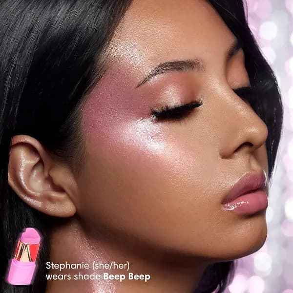 Model wearing Trixie Cosmetics cream highlighter in shade Beep Beep on the cheekbone with pink glossy lips