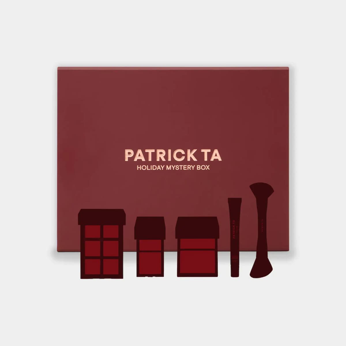 Patrick Ta Holiday Mystery Box in burgundy with rose-gold lettering, behind dark silhouettes of palettes, a tube and a brush