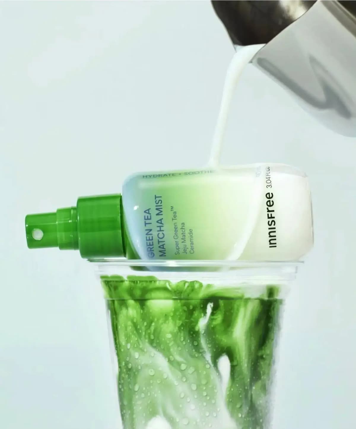 Innisfree Green Tea Matcha Mist bottle lying on a cup of iced matcha latte as milk pours over it from a steel pitcher